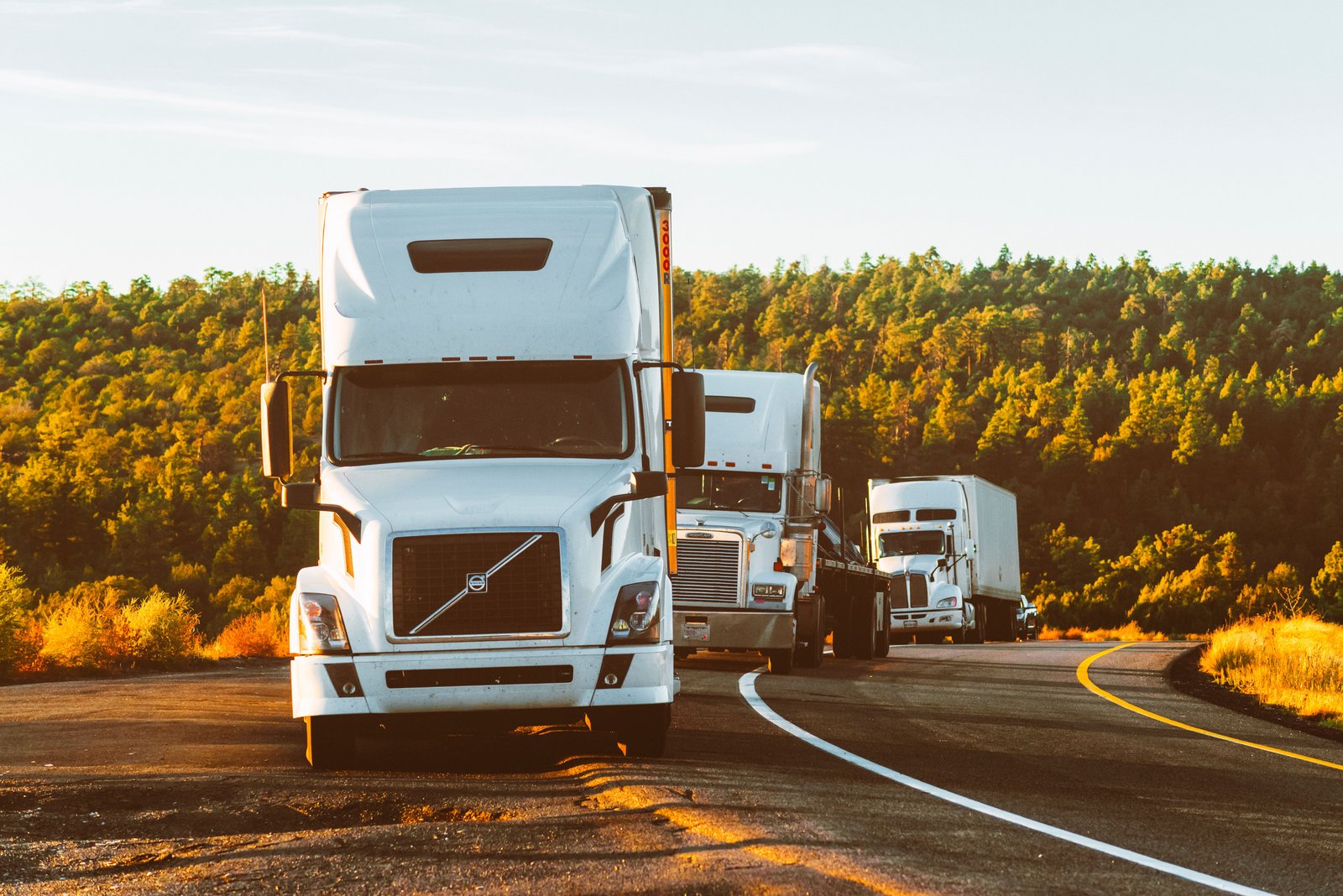 Three semi trucks on a mountain highway at sunset